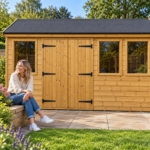 Front view of the Oakridge workshop double doors and windows, with a woman sitting on the garden wall beside it
